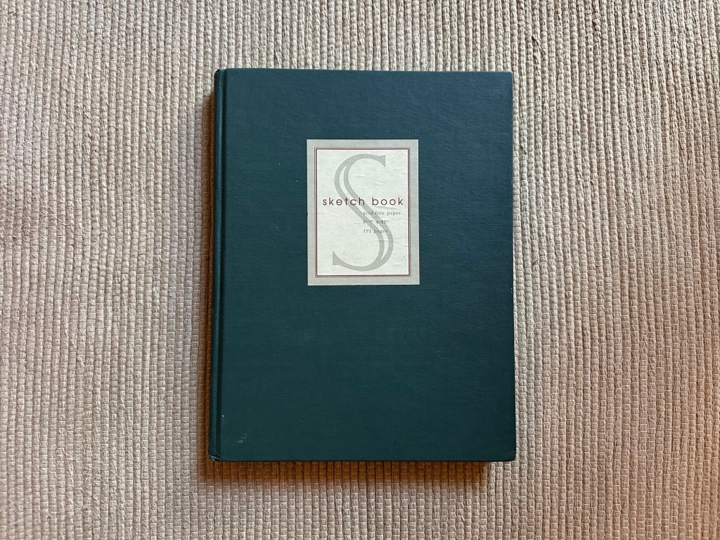 Closed green sketchbook on fabric yoga mat.